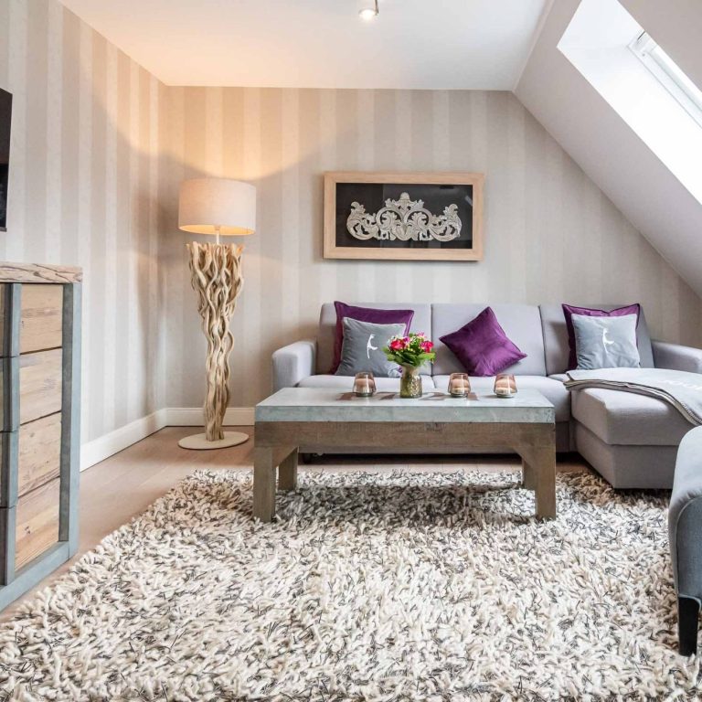 Im Hintergrund steht ein Sofa mit mehreren Kissen und davor steht ein passender Tisch mit Kerzengläser und Blumen