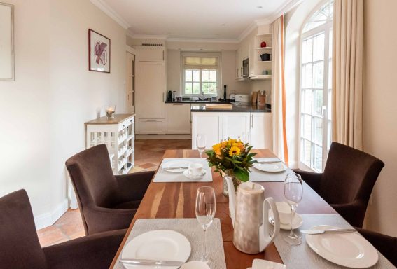 am gedeckten Tisch stehen vier Stühle mit Blick in die offene Küche
