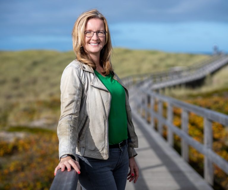 Die Fotografin Anne-Katrin Gerner lächelt in die Kamera und steht auf einem Weg, der zum Strand führt.