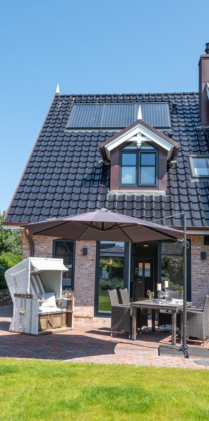 Auf der Terrasse des Hausteils steht ein Strandkorb mit Sitzgruppe und großem Sonnenschirm